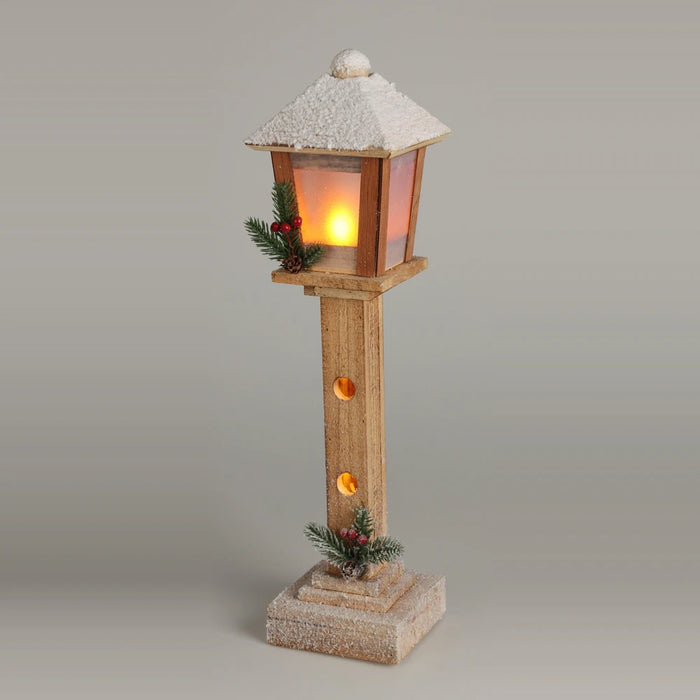 Wooden streetlamp with a snowy roof, glowing lantern and pine and berry sprigs