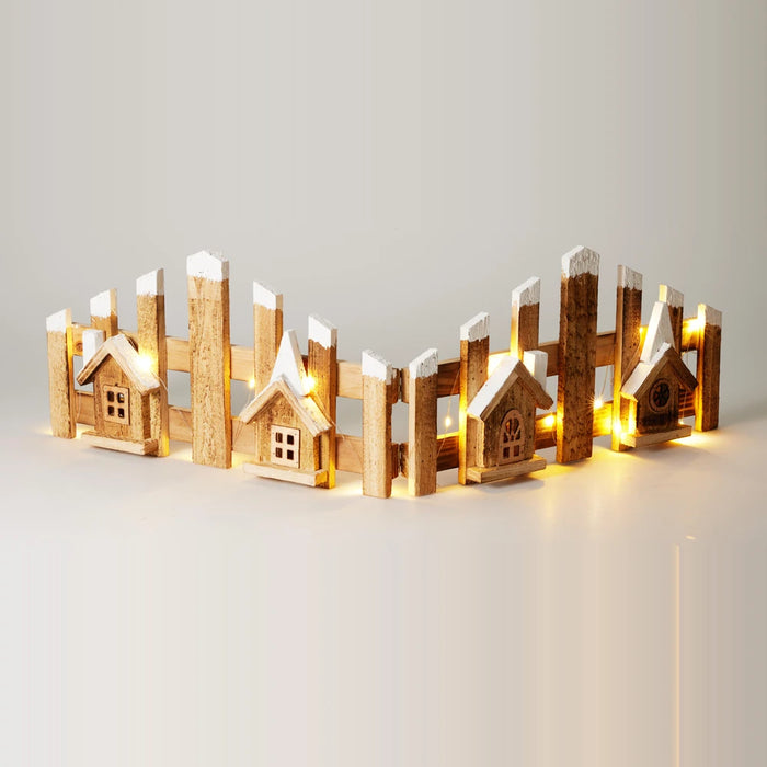 Snow-tipped wooden fence with four little wooden houses and warm fairy lights