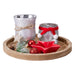 Round wooden tray with two frosted silver glass tealight holders, a red star dish, pine cone, snowy sprig and baubles