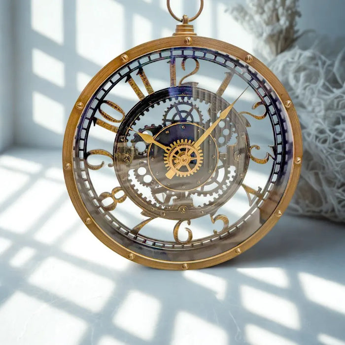 Industrial-style wall clock with a vintage brass-look finish and faux internal gears, hanging on a teal wall beside a mirror, styled in a showroom setting.