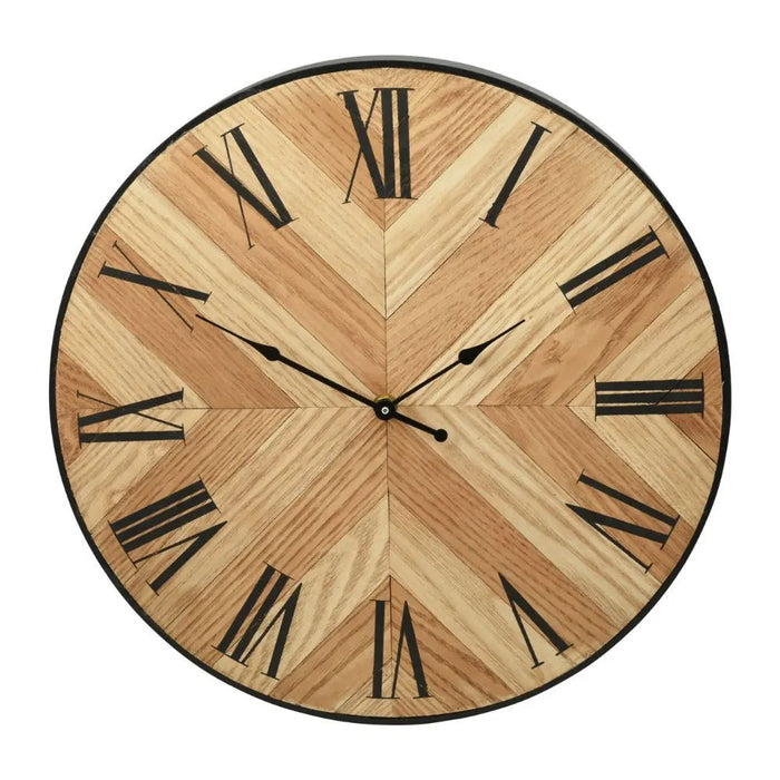 Chevron-patterned MDF clock with Roman numerals, styled on a round gold table against a dark feature wall with abstract artwork and modern glass wall lights.
