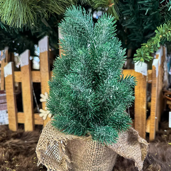Close-up of green Christmas tree branches in a burlap pot showing realistic pine needles and texture of the fabric base.