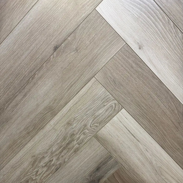 Close-up of Moon 12mm Herringbone laminate flooring showcasing cool wood tones and detailed grain texture.