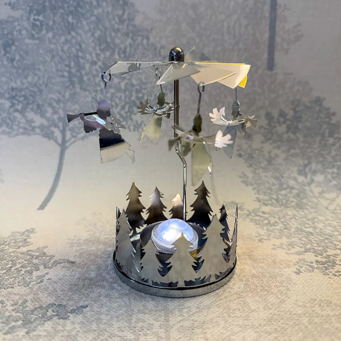Close-up of silver angel carousel tealight holder with angels spinning in warm candlelight.