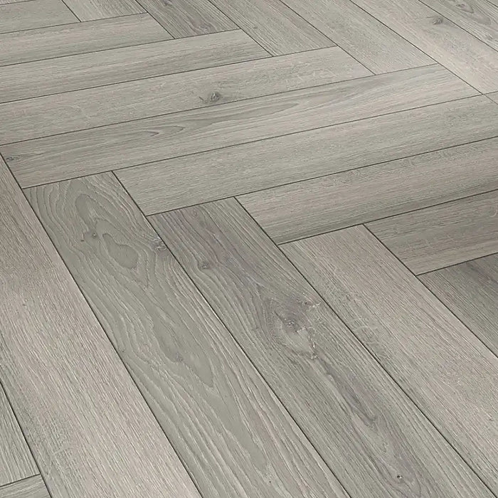 Close-up of Studioline Light Grey Herringbone laminate showing the natural matt finish, fine woodgrain detail, and bevelled plank edges.