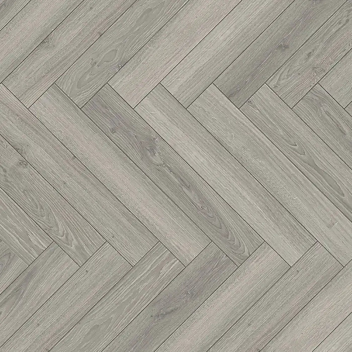 Close-up of Studioline Light Grey Herringbone laminate showing the natural matt finish, fine woodgrain detail, and bevelled plank edges.