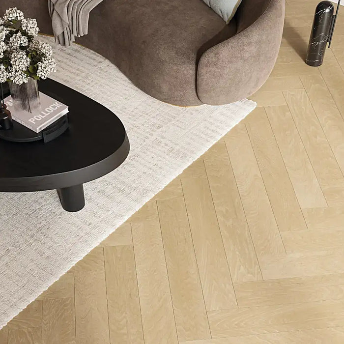 Natural oak herringbone laminate flooring styled in a warm, elegant living room, highlighting its realistic parquet look and golden-brown tones.