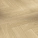 Close-up view of Studioline Natural Herringbone laminate showing its soft oak woodgrain detail and natural matt textured surface.