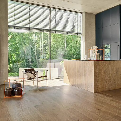 Wide plank Trendtime 4 Living Nougat engineered wood flooring in a modern, softly lit living room with natural textures and warm tones.