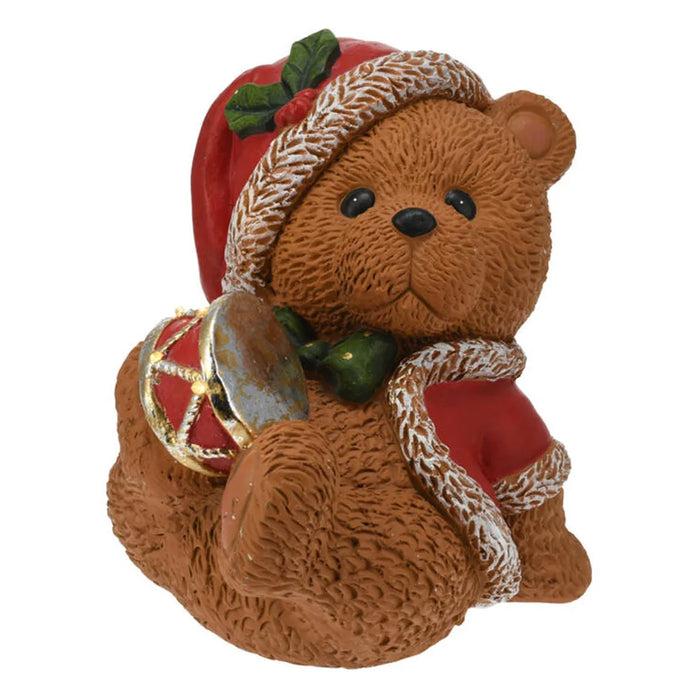 Sitting Christmas bear in a Santa hat playing a red and gold drum
