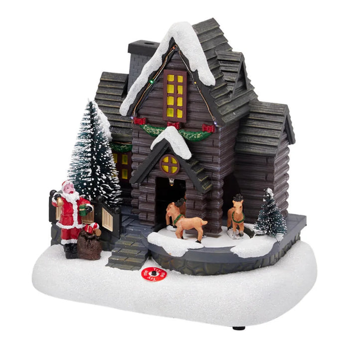 Brown log house scene with reindeer at the door, Santa by the steps and snowy trees on a white base
