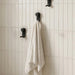 Nami adhesive hooks in black colour on white tile wall with towel
