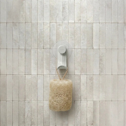 Nami adhesive hook in sand colour on tile wall holding a loofah