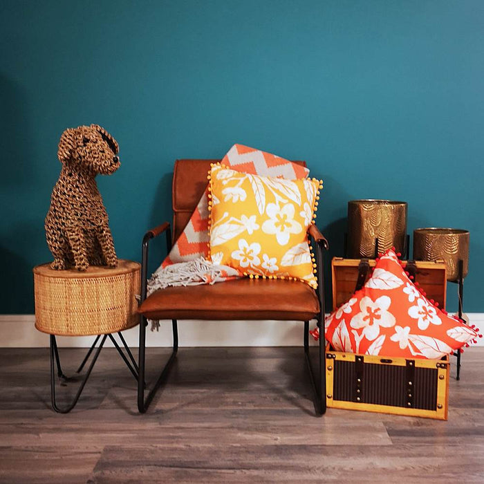 A living room setting with a brown leather chair and Hawaii vibrant orange floral print cushion with pom pom edging