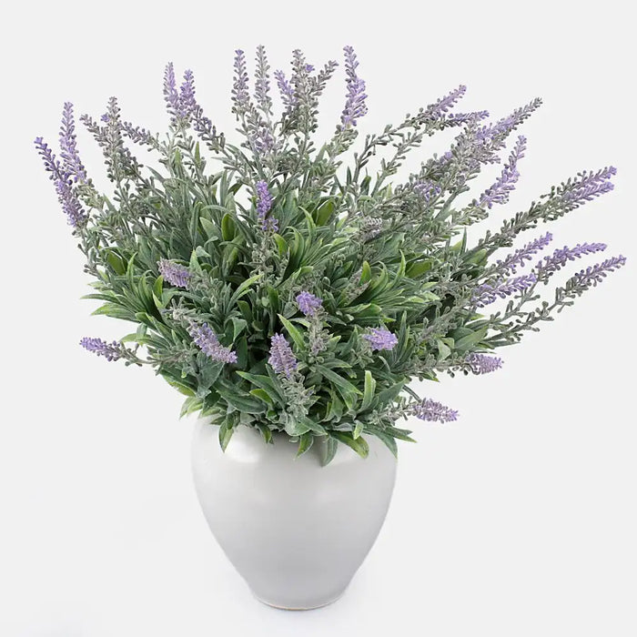 Artificial bush of violet lavender flowers with green leaves in a white vase